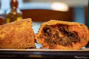 Pastel Brasileiro crocante crispy de carne desfiada com cheddar em mesa de restaurante com pimenta no fundo