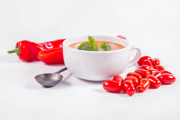 Gazpacho soup with some tomatoes and sweet pepper , decorated with fresh mint and black pepper on a white background with a vintage spoon
