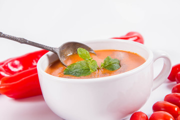 Gazpacho soup with some tomatoes and sweet pepper on a white background with a vintage spoon