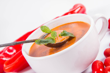 Gazpacho soup with some tomatoes and sweet pepper on a white background with a vintage spoon