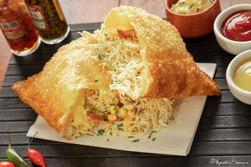 Pastel brasileiro frito com recheio de frando desfiado e milho  e queijo com requeijão encima de uma esteira preta com molho ketchup e mostarda e molho de pimenta 