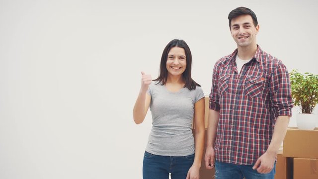 Pleased man and woman standing in new apartments, smiling. Man is showing keys, woman is giving thumb up.