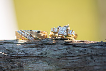 Gold wedding rings with  square diamonds side by side on wood log outdoors