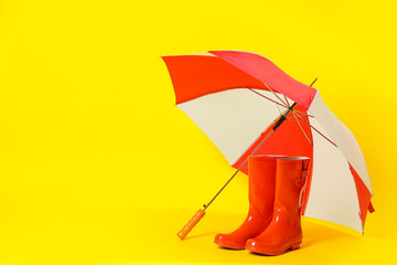 Colorful umbrella and red rubber boots on light yellow background. Space for text © New Africa