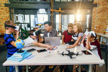 Preteen students using augmented reality for studying in modern smart school. Group of pupils with VR headsets during a computer science class.