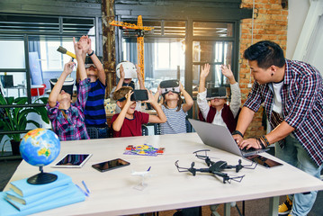 Korean scientist with the group of young pupils with laptop and VR headsets during a computer...