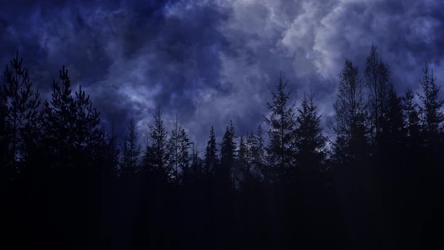 Dark blue and grey storm clouds passing over a misty forest silhouette.