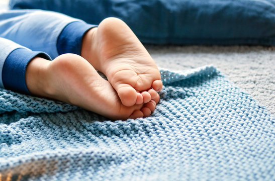 Cozy holidays at home. Close up photo of little child barefooted feet on blue knitted blanket lying on floor in pyjama. Winter season lifestyle. Leisure time. Sweet childhood. Copy space