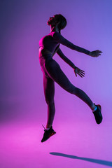 Fototapeta na wymiar Sporty young woman jumping isolated on purple light background
