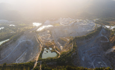 aerial drone Flying over the granite quarry among the forest , cranes and equipment for production of granite and marble. Quarry construction. Granite mining industry causes air pollution