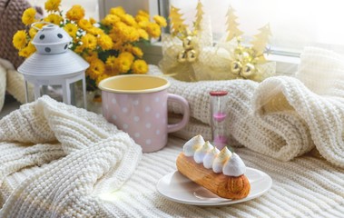 Still life of eclair, flowers, mugs, hourglass, candle holder, knitted fabric in the morning light.
