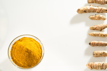 Stack of turmeric powder and turmeric rhizomes separate on a white background