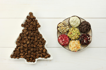 Roasted coffee beans in white dish-spruce, set of chocolates in white round saucer on white wooden background