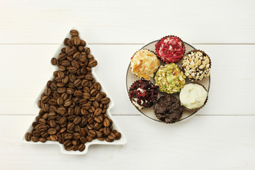 Roasted coffee beans in white dish-spruce, set of chocolates in white round saucer on white wooden background