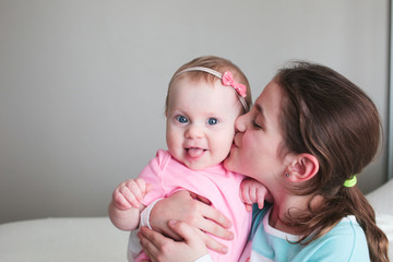 Close up Portrait of Two Sisters, Cute 8 Month Old baby Girl with Big blue Eyes and 8 Years Old School Age Girl With Brown Eyes , Happy Baby Girl