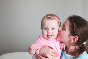 Close up Portrait of Two Sisters, Cute 8 Month Old baby Girl with Big blue Eyes and 8 Years Old School Age Girl With Brown Eyes , Happy Baby Girl