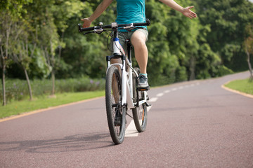 Woman cyclist riding mountain bike on tropical forest trail with arms outstretched