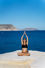 Young pregnant woman practicing yoga next to the mediterranean sea