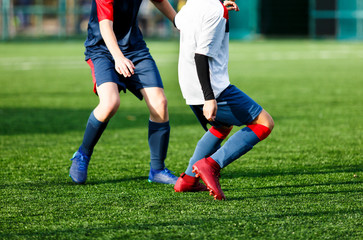 Fototapeta premium Boys in white and blue sportswear plays football on field, dribbles ball. Young soccer players with ball on green grass. Training, football, active lifestyle for kids concept 