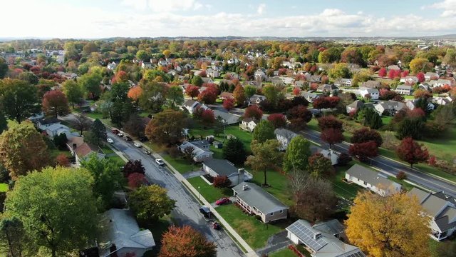 Aerial, cars are parked along a wide suburban street with homes on either side of the roadway, Lititz, Lancaster County, Pennsylvania, Autumn, fall colorful leaves, foliage