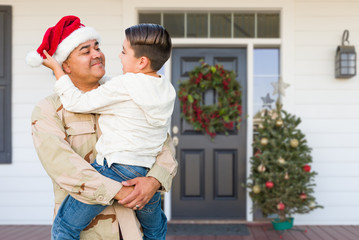 Hispanic Male Soldier Wearing Santa Cap Holding Mixed Race Son In Front of House