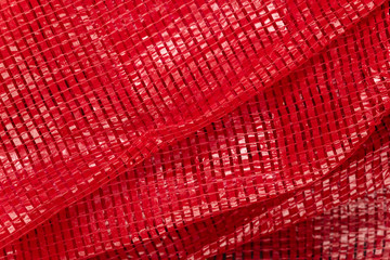 Red woven plastic net for packaging fruits, vegetables, or products. Abstract close-up background. Expanded polyethylene texture.