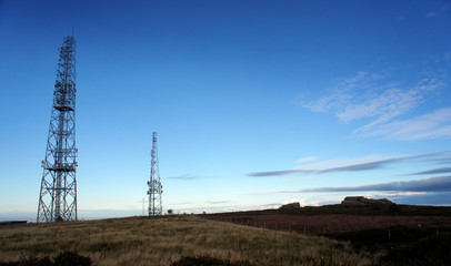 Slim silhouettes of telecommunication antennas in the evening sky.