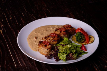 Pork medallions with vegetables on white plate, wooden background, dark light, angle view