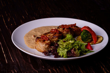Pork medallions with vegetables on white plate, wooden background, dark light, angle view