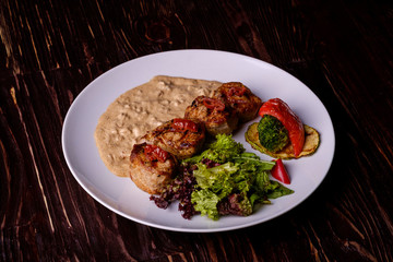 Pork medallions with vegetables on white plate, wooden background, dark light, angle view