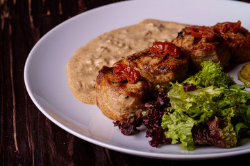 Pork medallions with vegetables on white plate, wooden background, dark light, angle view