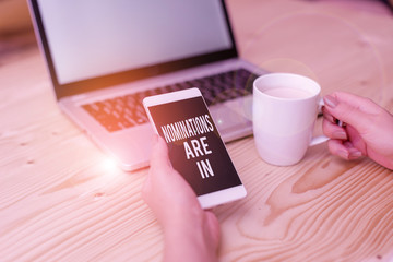 Writing note showing Nominations Are In. Business concept for Formally Choosing someone Official Candidate for an Award woman with laptop smartphone and office supplies technology