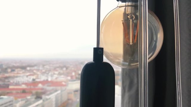 Yellow vintage light bulbs hanging in front of the window with a big city in the background. Hanging retro light bulbs. Buildings inspirational ideas for electricity of alternative solar energy.
