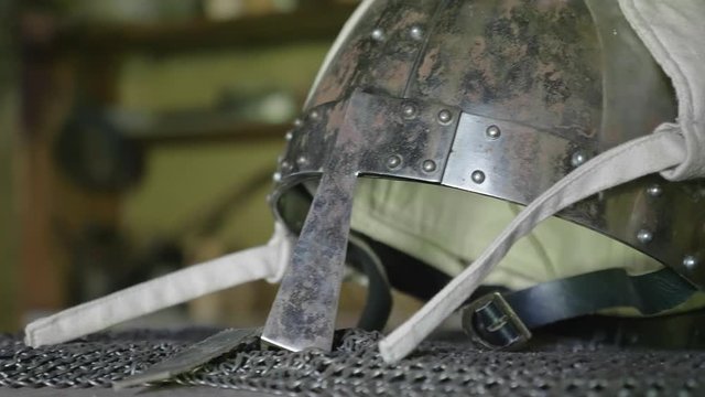 Panning closeup shot of medieval helmet on wooden bench.
