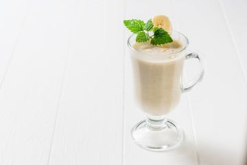 Glass glass with oatmeal-banana smoothie and mint on a white table. Vegetarian smoothie.