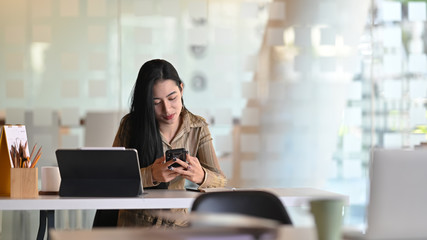 Fototapeta na wymiar Young female using smartphone on modern office.
