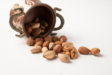 Almonds, hazelnuts, pecan nuts, pistachio nuts on a white surface in an old vintage small bucket