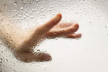 Fototapeta premium hand of a young woman behind glass with water drops on it reaching out