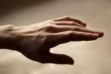 hand of a young woman reaching out on beige background - obrazy, fototapety, plakaty