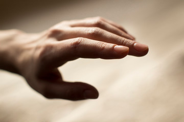 hand of a young woman reaching out on beige background - obrazy, fototapety, plakaty