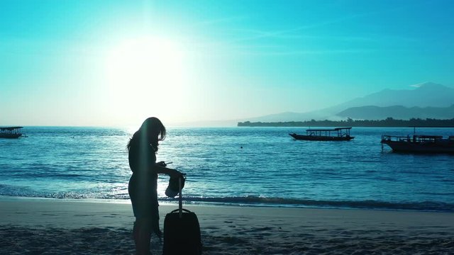 Arrival at the tropical destination. silhouette of the woman with the luggage. removing hat and checking a map on the smartphone