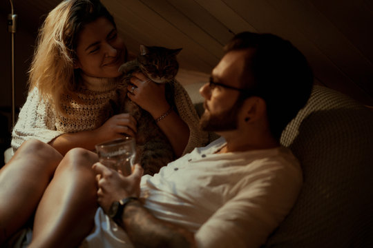 Young Couple In Love Spends A Cozy Evening At Home On The Couch With A Cat.