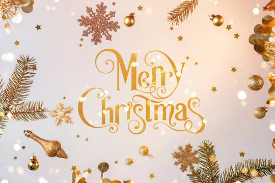 Merry Christmas text with gold flying decorations, gift boxes, fir branches, snowflakes, sparkles and confetti on light gold background. Xmas and New Year holiday, bokeh, light. Selective focus