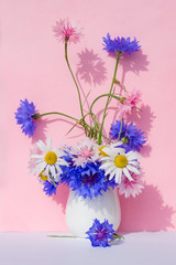 Bouquet of blue, pink wild flowers cornflower in a vase on a background of colored paper . Summer, spring background
