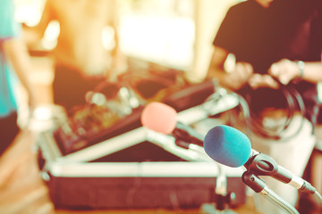 Two microphones with blue and red sponges placed on a stand with earphones on the table with blur image of the audio technician was installing and testing the sound system in the background.