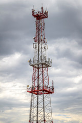 A large red and white cell tower against a gray cloudy sky.