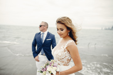 Beautiful bride in a long white dress. Handsome fiance in a blue suit. Couple near ocean