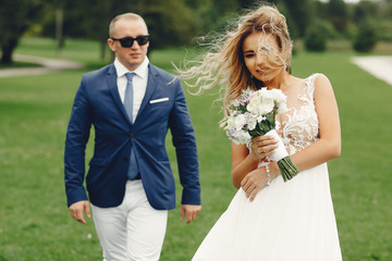 Beautiful bride in a long white dress. Handsome fiance in a blue suit. Couple in a summer park
