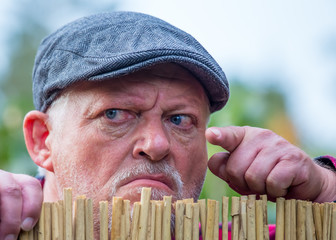 Close-up of a senior man with flat cap. He looks grim and aggressive. Concept: neighborhood and...