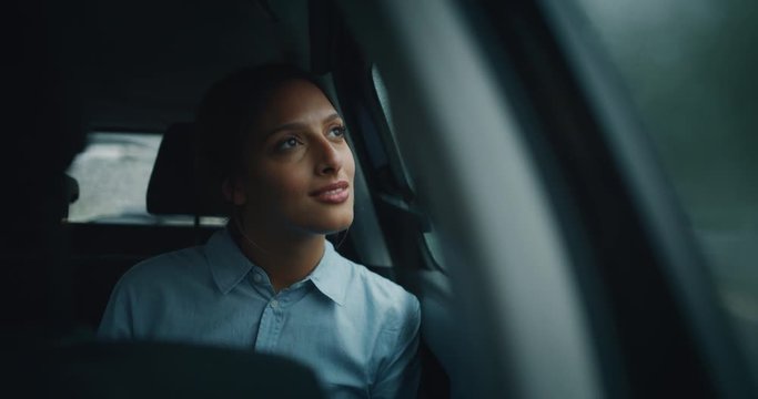 An young businesswoman is driving a modern car in a center of the city by night while is raining outside.